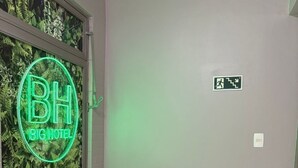A hotel room with a green neon sign, a white furry chair, a tiled floor, and a wall with a leafy pattern. - Big Hotel - Florianopolis continental (Florianopolis)