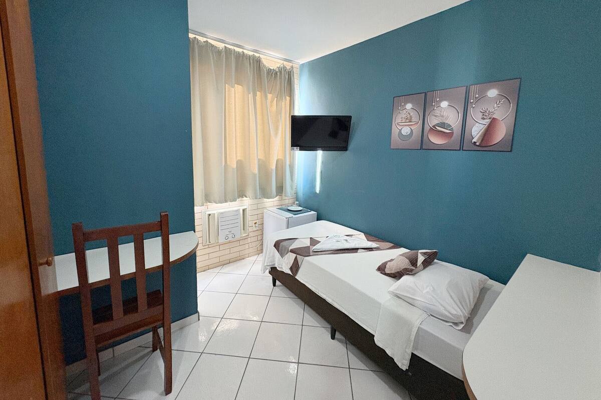 Un dormitorio con cama, escritorio, silla, televisor y ventana con cortinas.