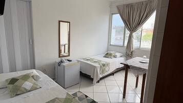 Une chambre d’hôtel avec deux lits, un bureau, une chaise, un ventilateur de plafond, une fenêtre avec des rideaux et une vue sur la ville.