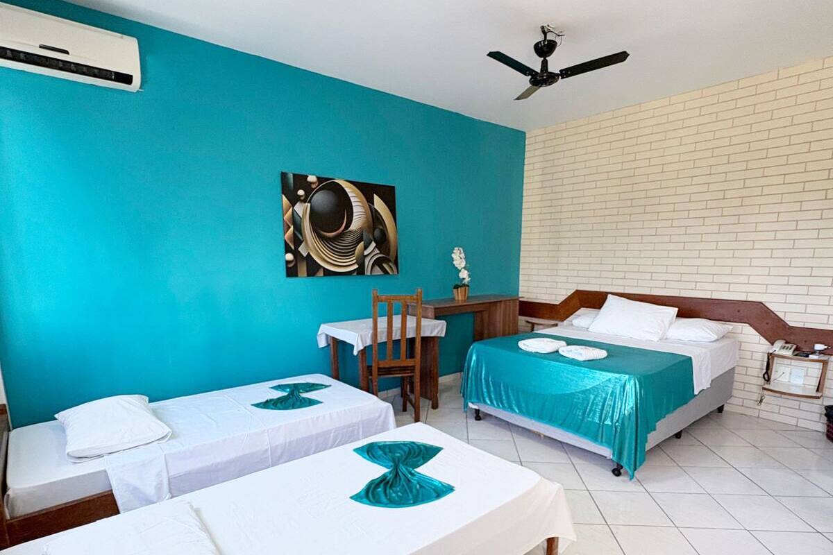 Habitación de hotel con dos camas, un escritorio, una silla, un ventilador de techo y aire acondicionado instalado en la pared.
