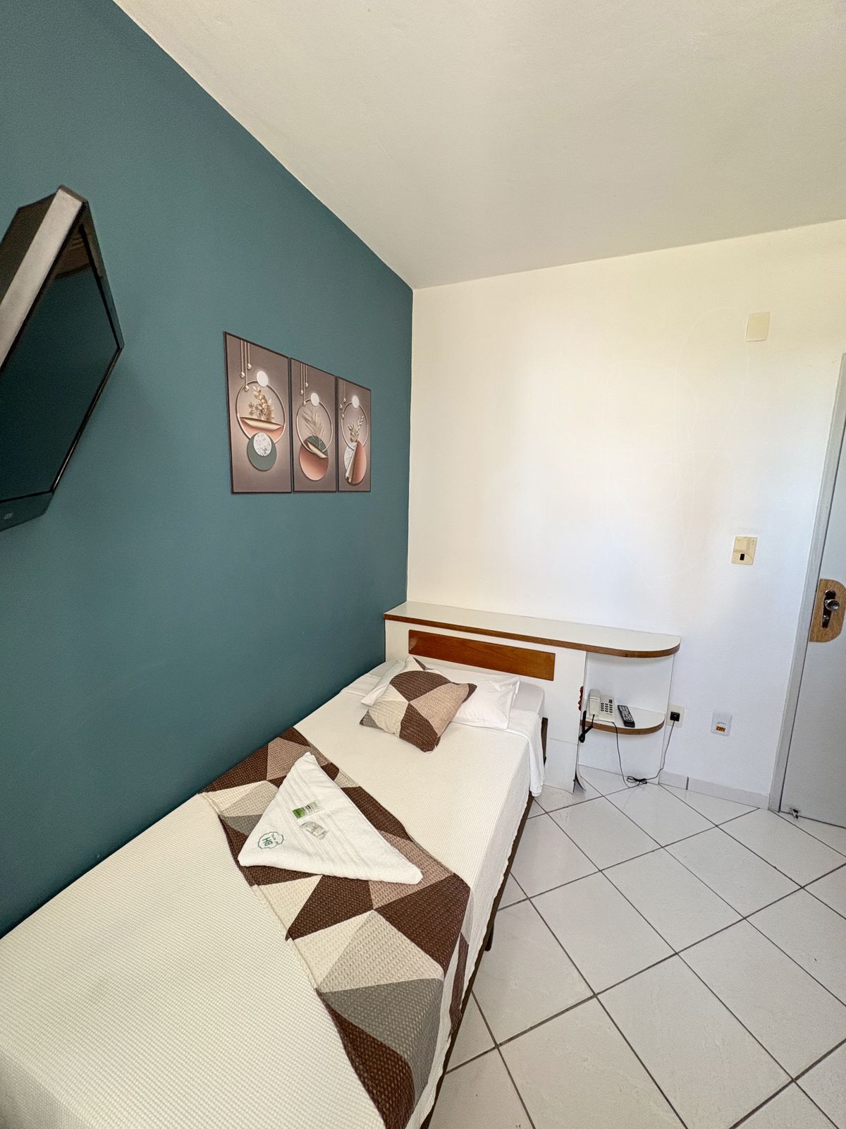 Ein Zimmer mit einem Einzelbett, einem Schreibtisch, einem Flachbildfernseher und Bildern an der Wand.