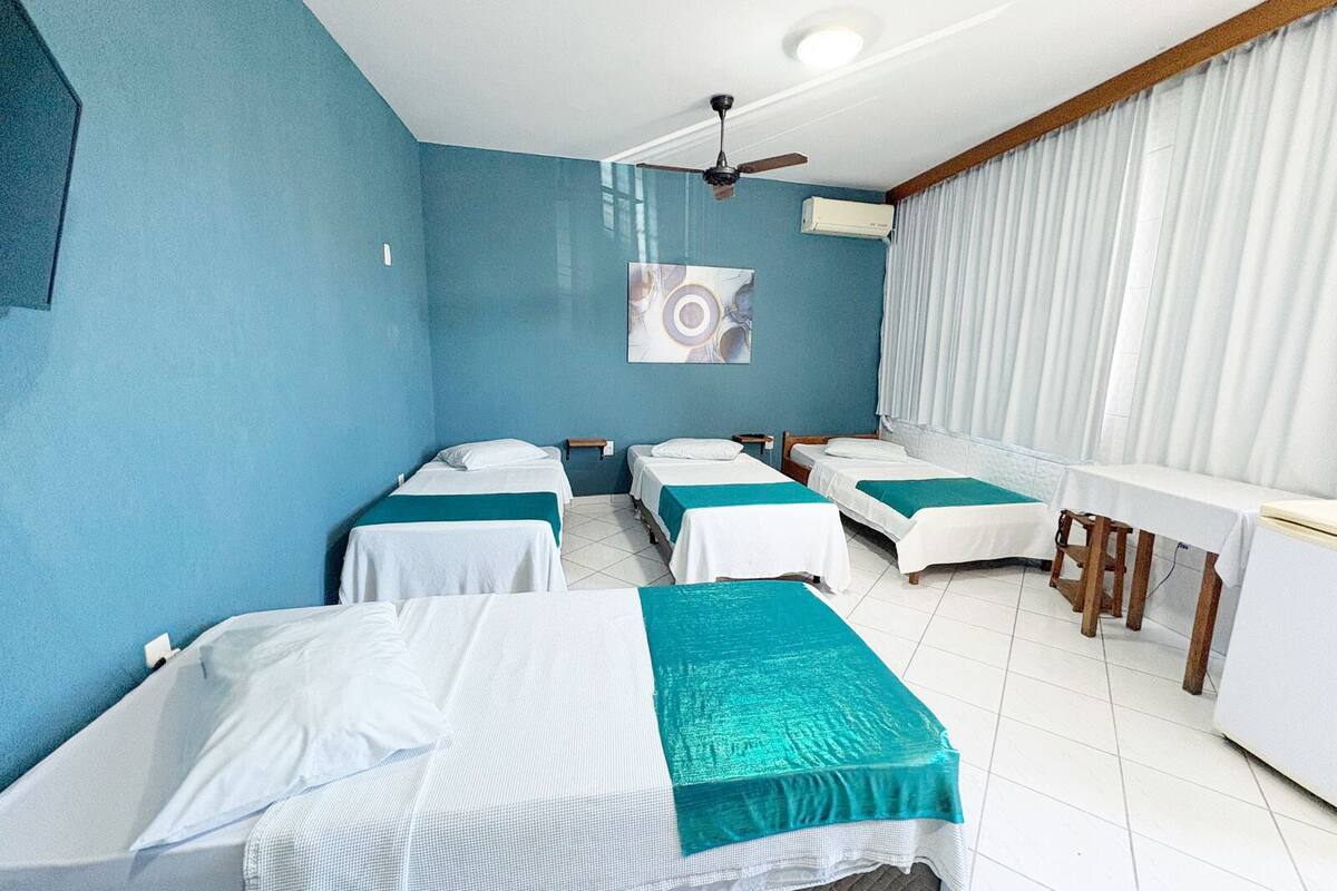 Una habitación de hotel con cuatro camas individuales, un escritorio, un ventilador de techo y aire acondicionado.