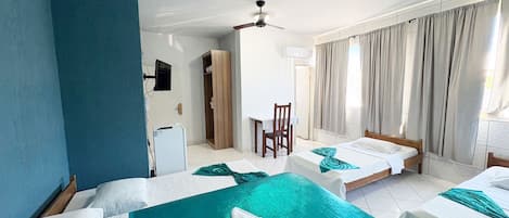 Une chambre d’hôtel avec deux lits, un bureau, une chaise, un ventilateur de plafond et une vue sur l’extérieur.