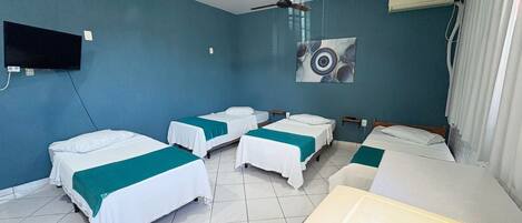 Habitación de hotel con cuatro camas individuales, ventilador de techo, televisor montado y un cuadro en la pared.