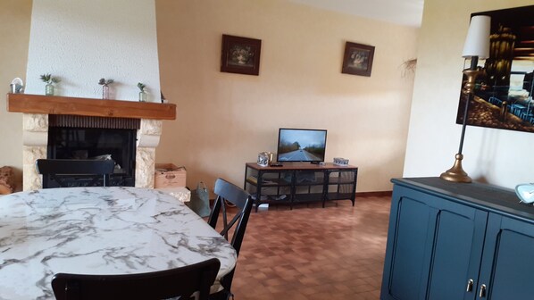 A living room with a fireplace, a television, a dining table, and a blue cabinet. - The LEON House (Ychoux)