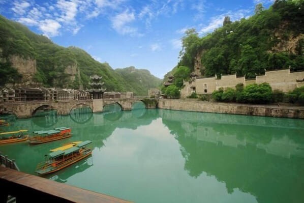 A serene river with traditional boats, a stone bridge, and ancient architecture amidst lush greenery. - Dahe Guanyi Inn (Zhenyuan County)