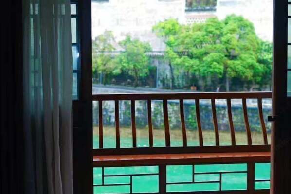 A view through a window with a wooden railing, a green outdoor area, and a building in the background. - Dahe Guanyi Inn (Zhenyuan County)