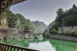 A traditional Chinese courtyard with a bridge over a calm river, surrounded by lush greenery and historic buildings. - Dahe Guanyi Inn (Zhenyuan County)