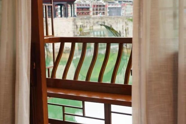 A view through a window with a wooden railing, a green outdoor area, and buildings in the background. - Dahe Guanyi Inn (Zhenyuan County)