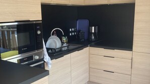 Uma cozinha moderna com armários de madeira clara, bancada preta, micro-ondas Bosch, cafeteira e eletrodoméstico azul.