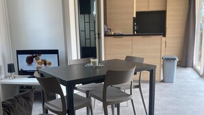 Uma sala de estar moderna com uma mesa de jantar, cadeiras, uma TV e uma cozinha com armários de madeira e uma janela.
