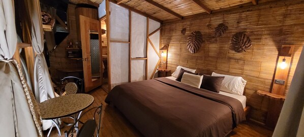 A cozy room with a bed, a small table, and a chair. There is a wooden wall with leaf decorations and a light fixture. - Exclusivo Cocora con jacuzzi salento (Salento)