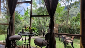 A room with a large window overlooking a lush garden. There is a round table with two chairs and a small table with two wine glasses and cups. - Exclusivo Cocora con jacuzzi salento  (Salento)