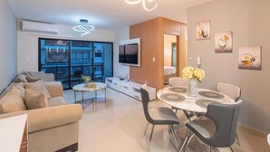 A modern living room with a sofa, dining table, and chairs, a TV mounted on the wall, and artwork on the walls.