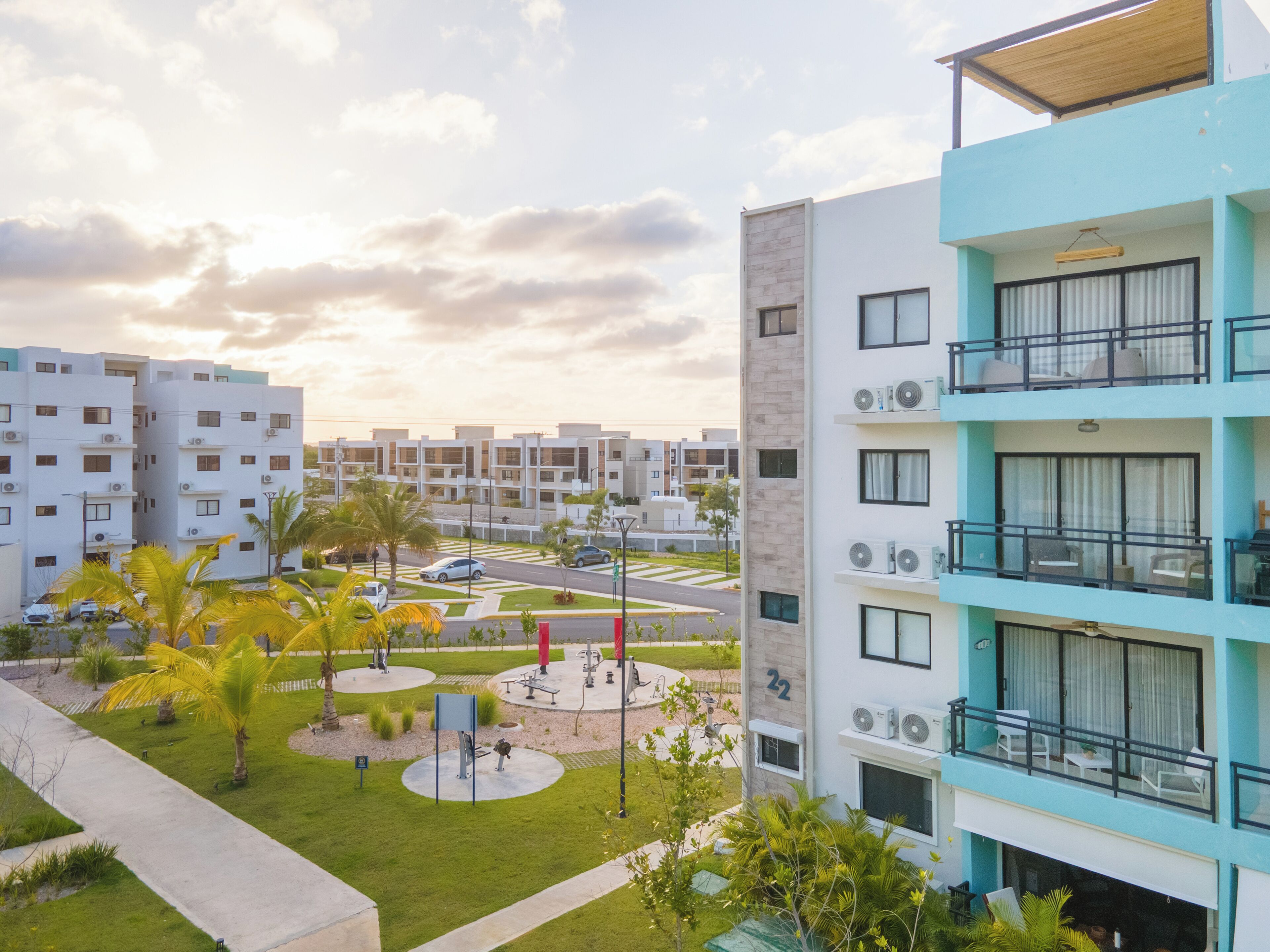 Un moderno edificio residenziale con numerosi balconi, un cortile curato con palme e una vista aperta sulla zona circostante.