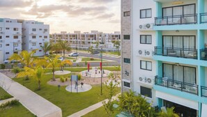 A modern apartment building with multiple balconies, a well-maintained courtyard with palm trees, and a clear view of the surrounding residential area.