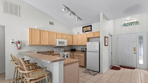A kitchen with wooden cabinets, a microwave, a refrigerator, a coffee maker, and a bar stool. - 3-bedroom villa in fantastic Clermont that backs on to a Conservation Area (Clermont)