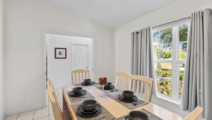 A dining area with a table set for four, chairs, a window with curtains, and a door with a framed picture. - 3-bedroom villa in fantastic Clermont that backs on to a Conservation Area (Clermont)