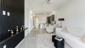 A modern living room with a white sofa, a black coffee table, and a kitchen area in the background. - Lux Design Apartment near beach (Fort Lauderdale)