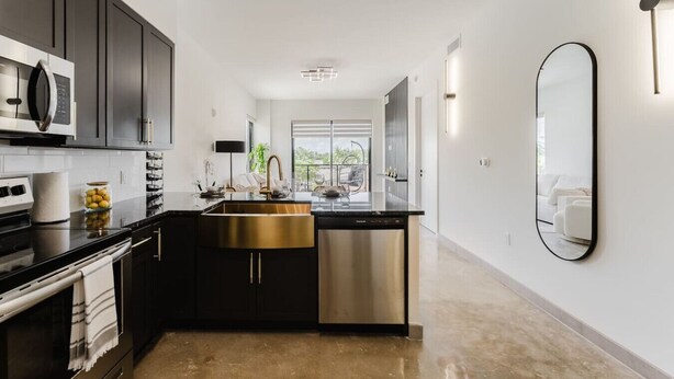 A modern kitchen with dark cabinetry, stainless steel appliances, and a gold-colored sink. - Lux Design Apartment near beach (Fort Lauderdale)