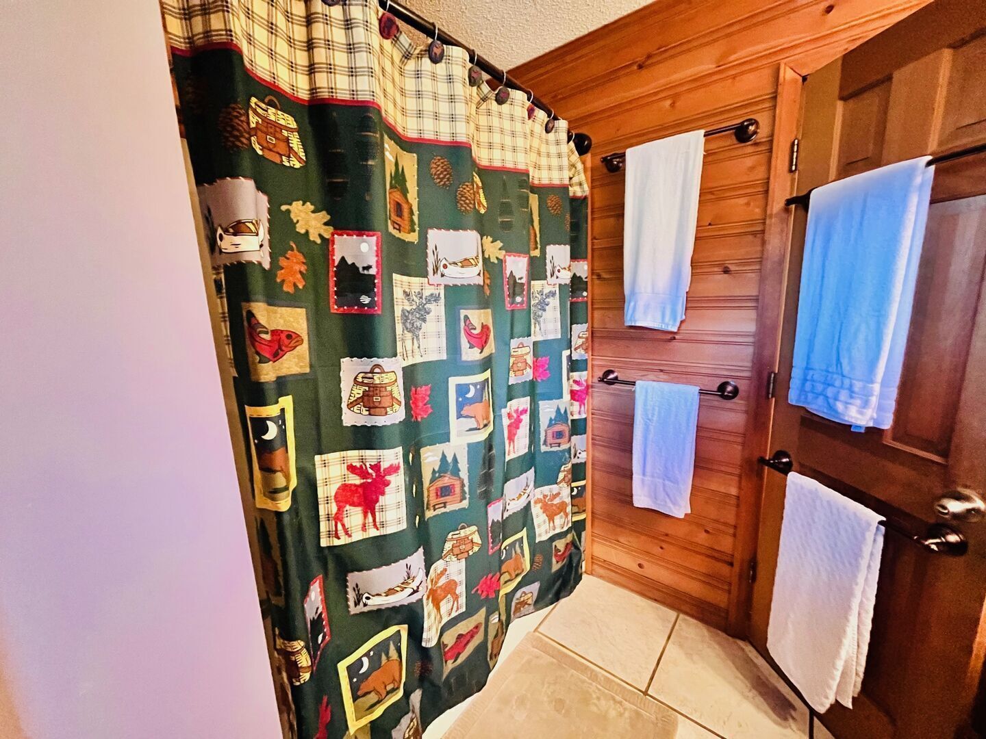 Un baño con cortina de ducha a cuadros, puerta de madera y varios toallas en un perchero.