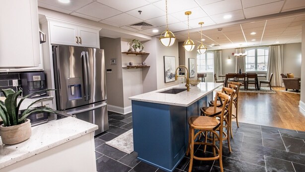 Een moderne keuken met een centraal eiland, roestvrijstalen apparatuur en een eethoek met houten stoelen en een tafel.