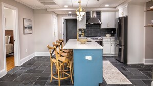 Een moderne keuken met een centraal eiland, barstoelen, een kroonluchter en een grote koelkast.