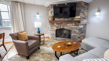 A living room with a stone fireplace, leather armchairs, a round coffee table, and a view through a large window.
