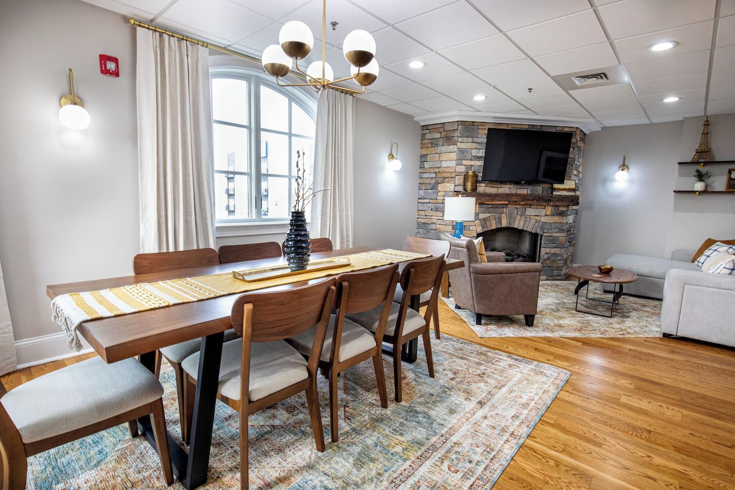 A dining area with a wooden table and chairs, a stone fireplace, and a television mounted on the wall.