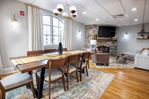 A dining area with a wooden table and chairs, a stone fireplace, and a television mounted on the wall.