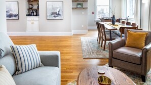 Een moderne woonkamer met een grijze bank, een houten salontafel en een eethoek met een tafel en stoelen.