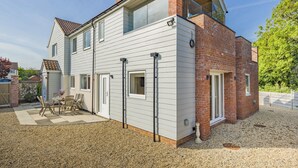 A two-story house with a sloped roof, a brick section, and a gravel driveway.