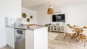 Een moderne keuken met een centraal eiland, een eetgedeelte met houten stoelen en een flatscreen televisie aan de wand.
