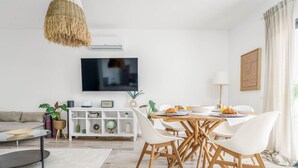 Een moderne woonkamer met een eethoek, witte meubels, een flatscreen televisie en een whiteboard aan de muur.
