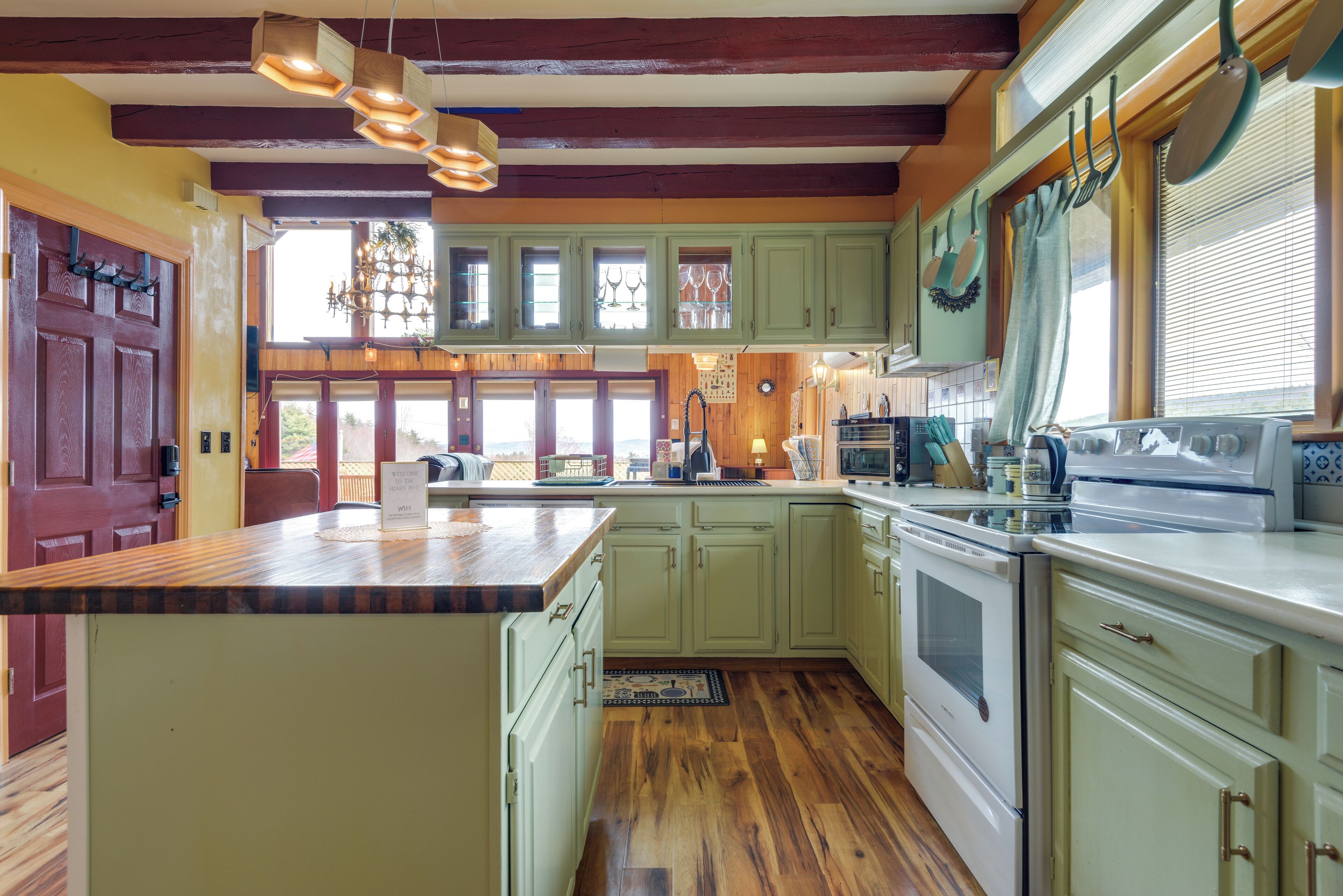 A kitchen with wooden floors, green cabinets, a large island, and a hanging light fixture.
