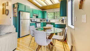 Een moderne keuken met blauwgroene kastjes, een glazen eettafel en een roestvrijstalen koelkast.