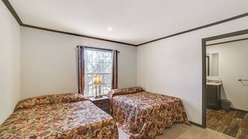 Une chambre avec deux lits, une fenêtre avec des rideaux, une table de chevet avec une lampe, et une vue sur une salle de bain par une porte ouverte.