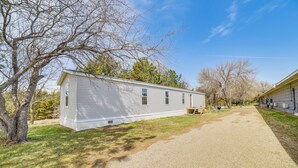 A single-story mobile home with a gravel driveway, surrounded by trees and a clear sky. - Dog-Friendly Miller Hunting Retreat! (Miller)