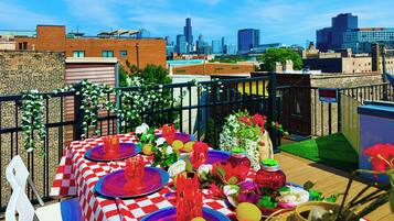 A rooftop dining area with checkered tablecloths, red and blue plates, and a city skyline in the background.