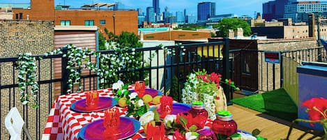 A rooftop dining area with checkered tablecloths, red and blue plates, and a city skyline in the background.