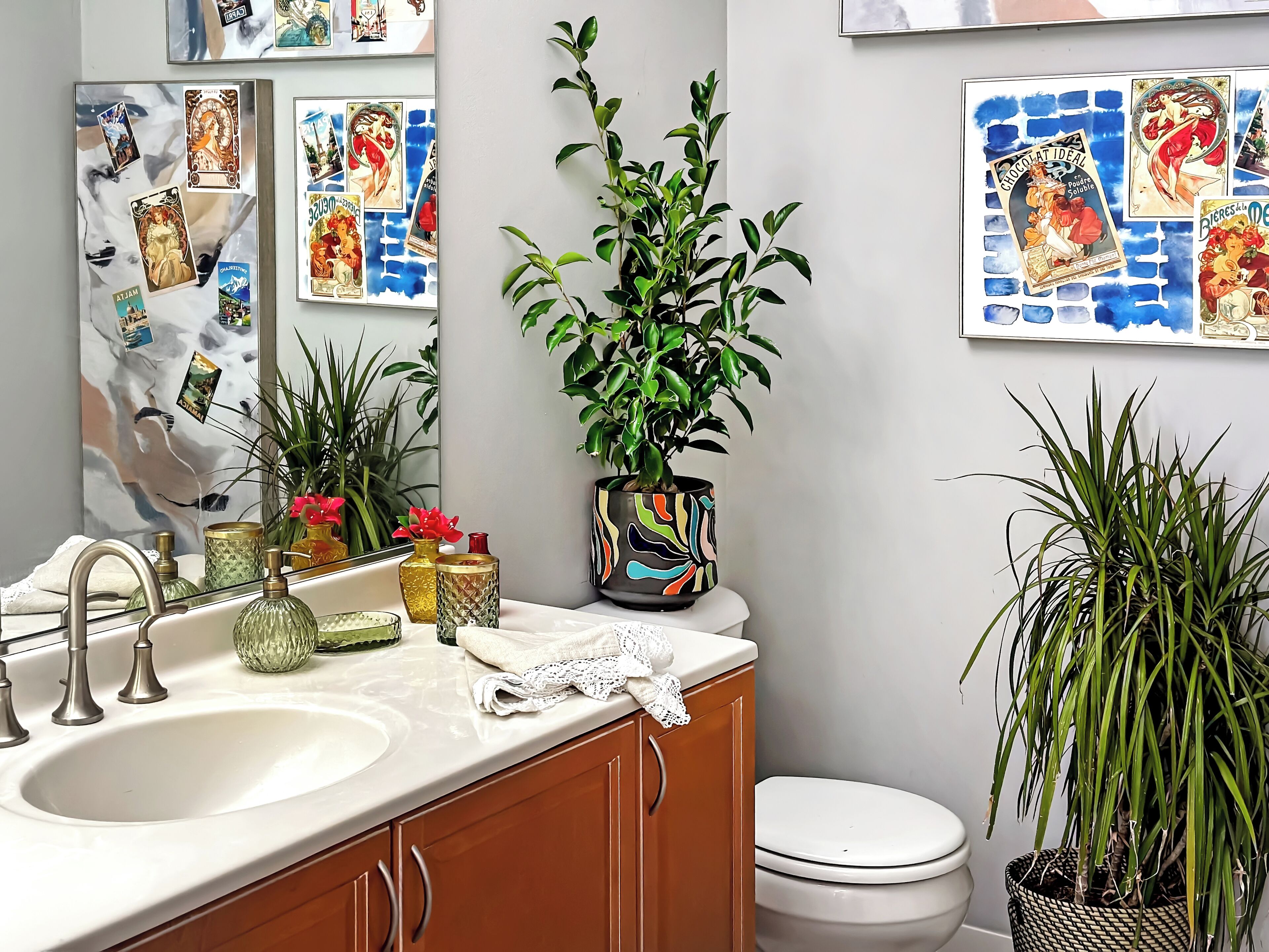 A bathroom with a white sink, a mirror, a toilet, and various decorative items including plants and framed pictures on the wall.