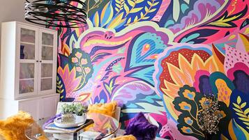 A room with a colorful mural, a glass table with a plant, and a white cabinet.