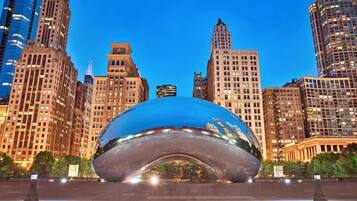 A large, reflective metallic sculpture in an urban setting with tall buildings in the background.