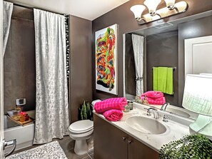 Features a sleek design with a large mirror, dual sinks, and a toilet, plus a vibrant abstract painting on the wall.