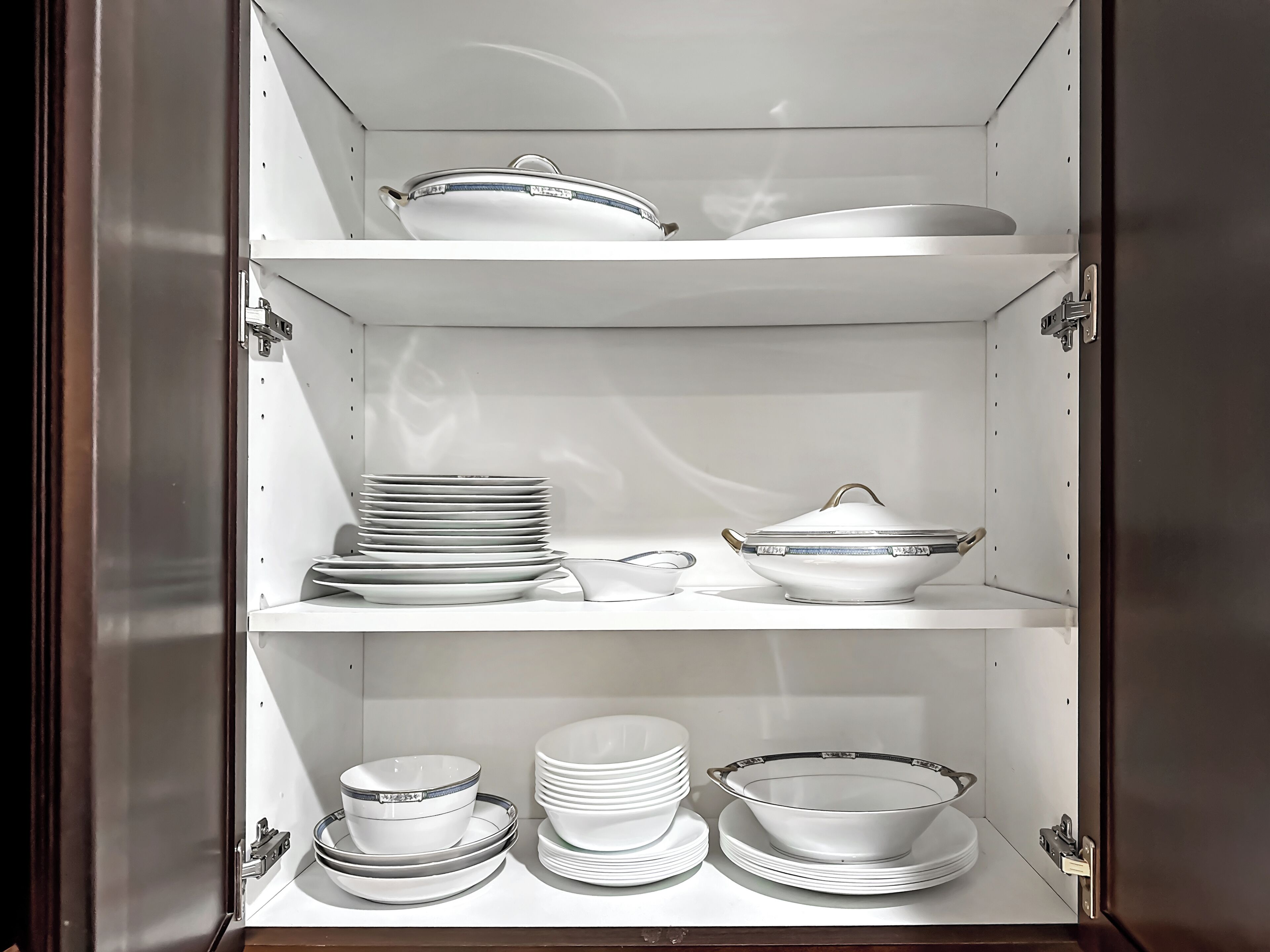 A kitchen cabinet with three shelves, each holding various kitchenware items.