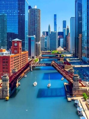 Experience the blend of old and new architecture in this vibrant waterfront city, with a historic clock tower and modern skyscraper overlooking a scenic waterway dotted with small boats.