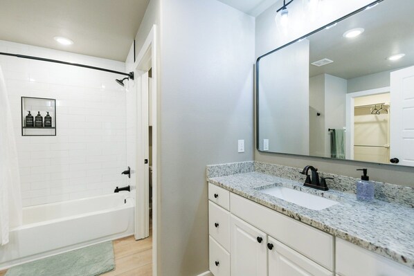 A modern bathroom with a white bathtub, a granite countertop sink, and a large mirror.