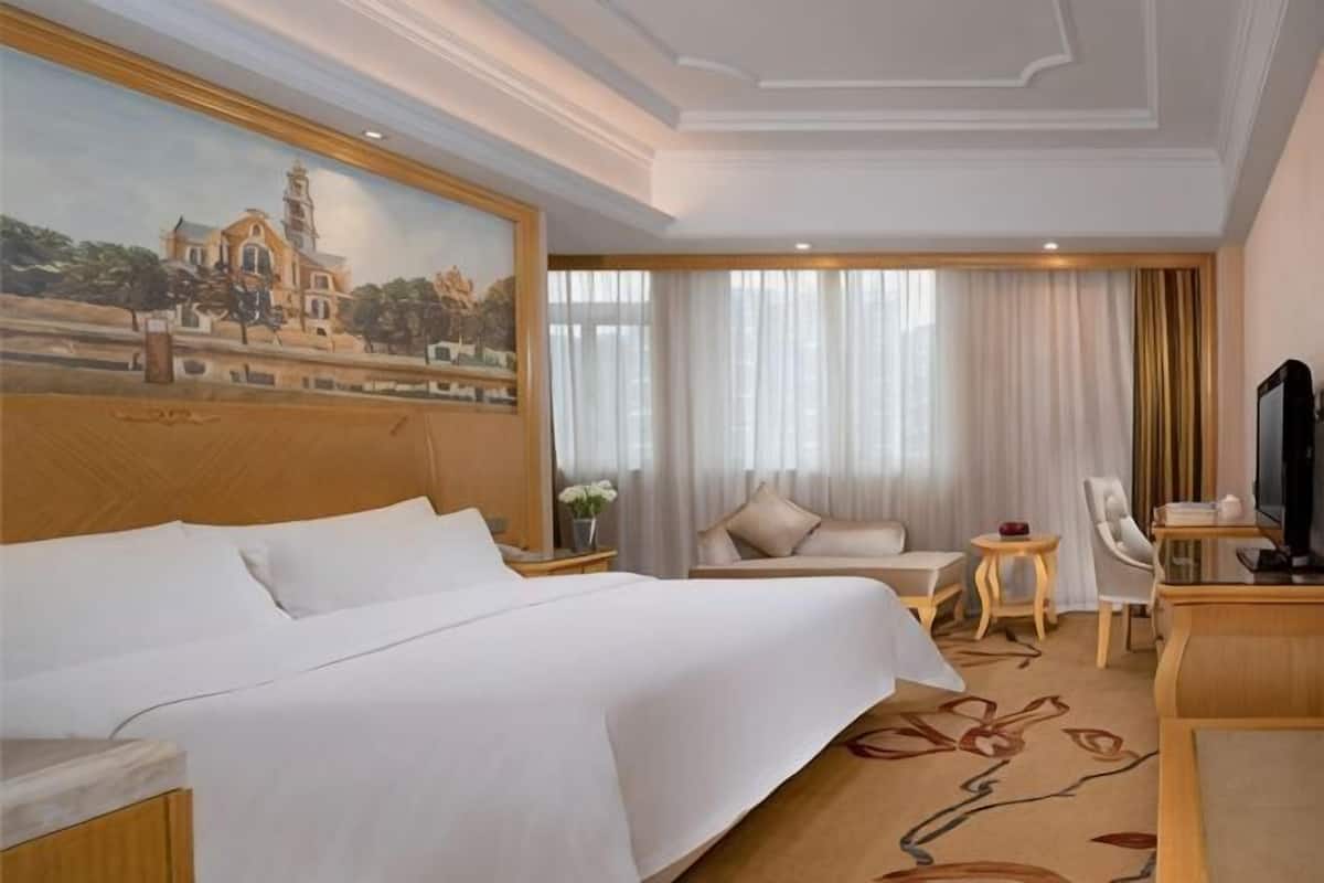 A hotel room with a large bed, a desk, a chair, a television, and a painting on the wall.