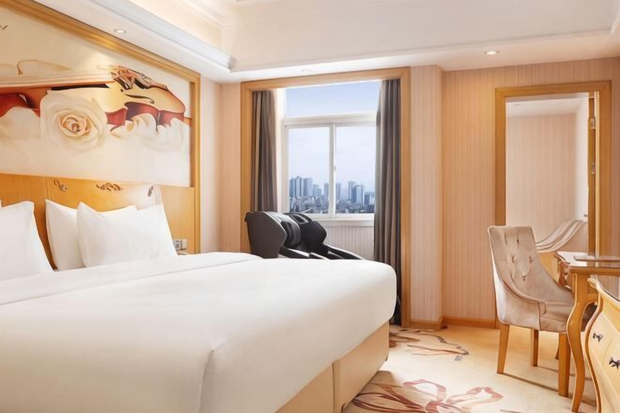 Une chambre d’hôtel avec un grand lit, un bureau avec une chaise, une vue sur la ville et un tableau au mur.