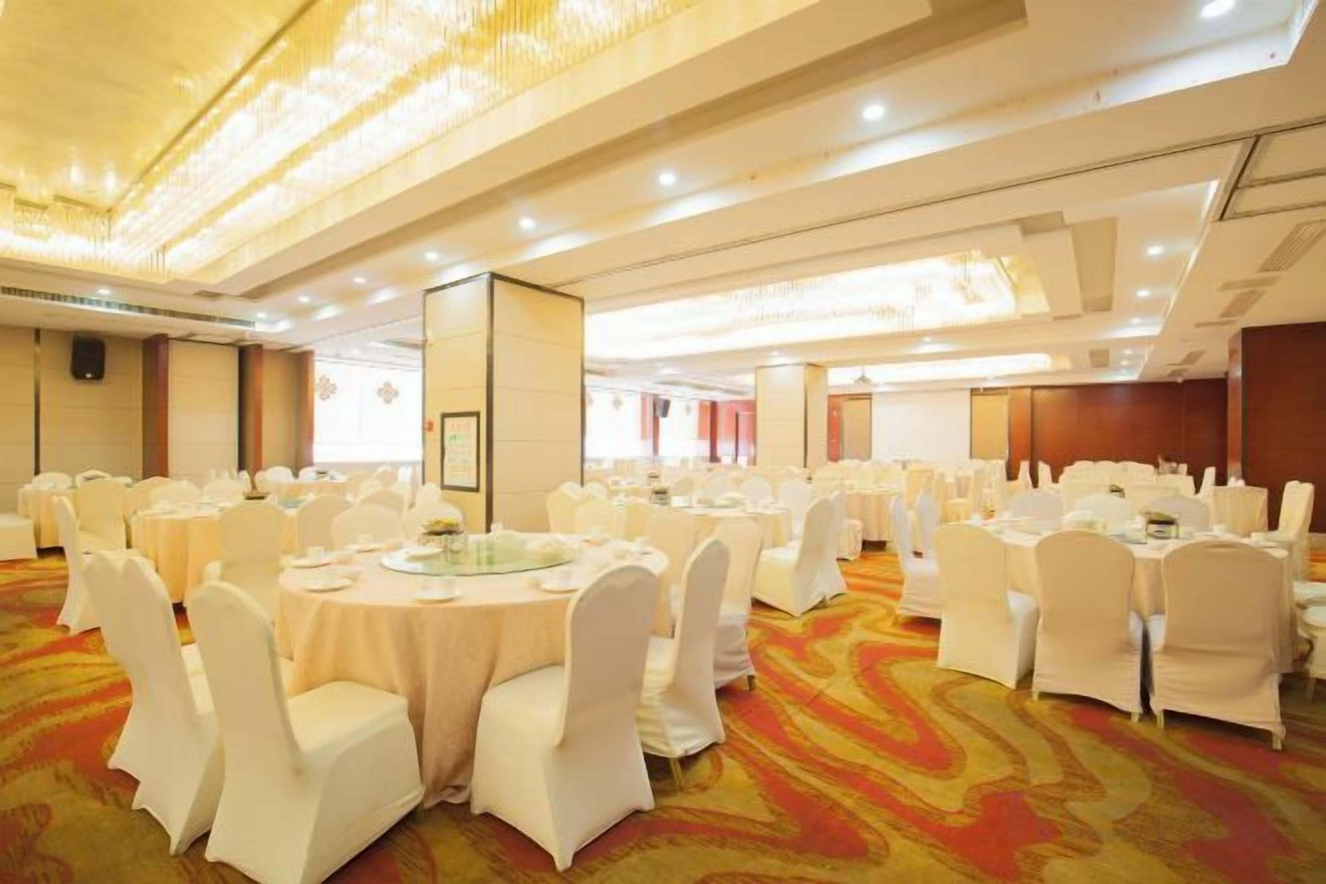 A banquet hall with round tables, white chairs, and a carpeted floor.